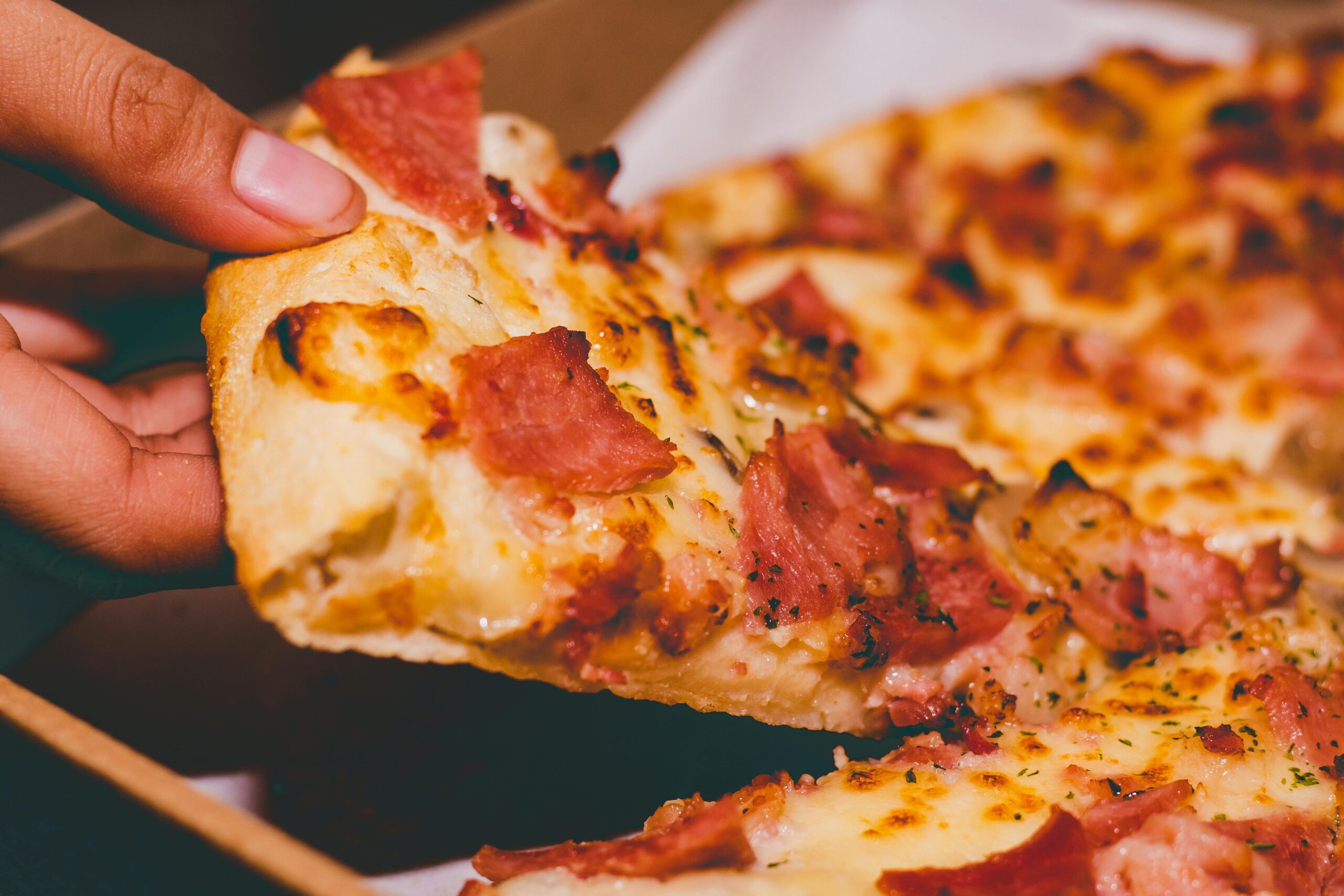 Close-up of a hand holding a delicious slice of pepperoni pizza.