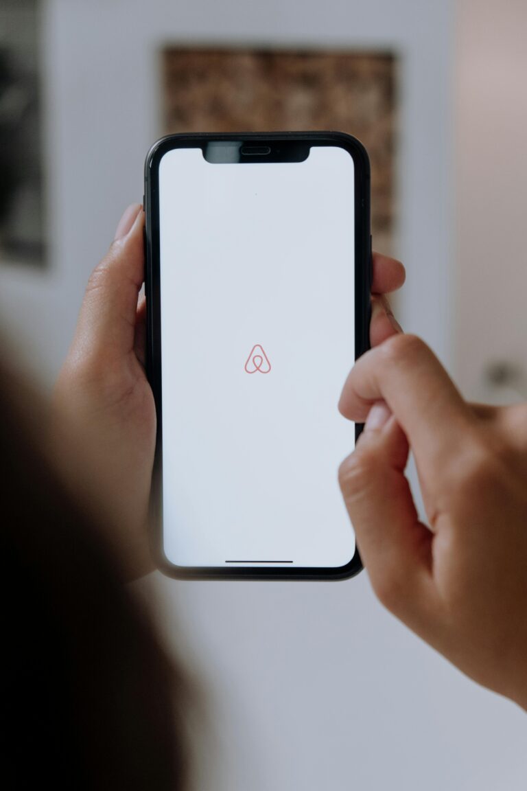 Close-up of hands holding a smartphone with Airbnb app logo on the screen indoors, highlighting modern technology.